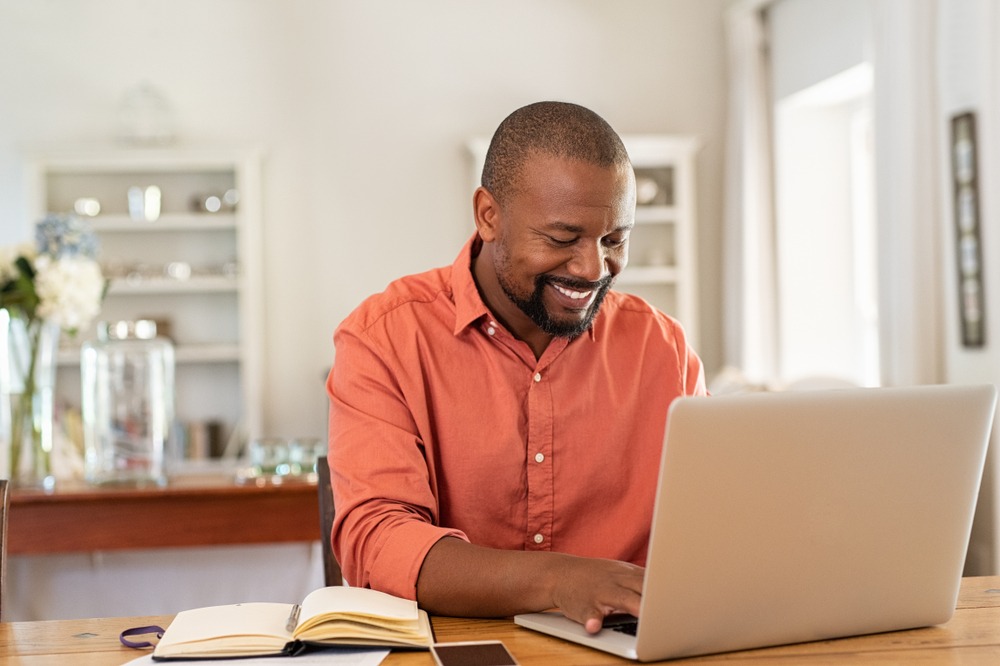 Smiling,Black,Man,Using,Laptop,At,Home,In,Living,Room.